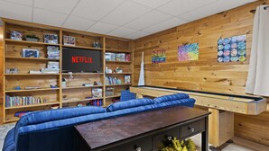 A room with a pool table, a sofa, and a bookshelf filled with games and books. - Mountain Views w Slide Hot Tub Game Room (Mineral Bluff)