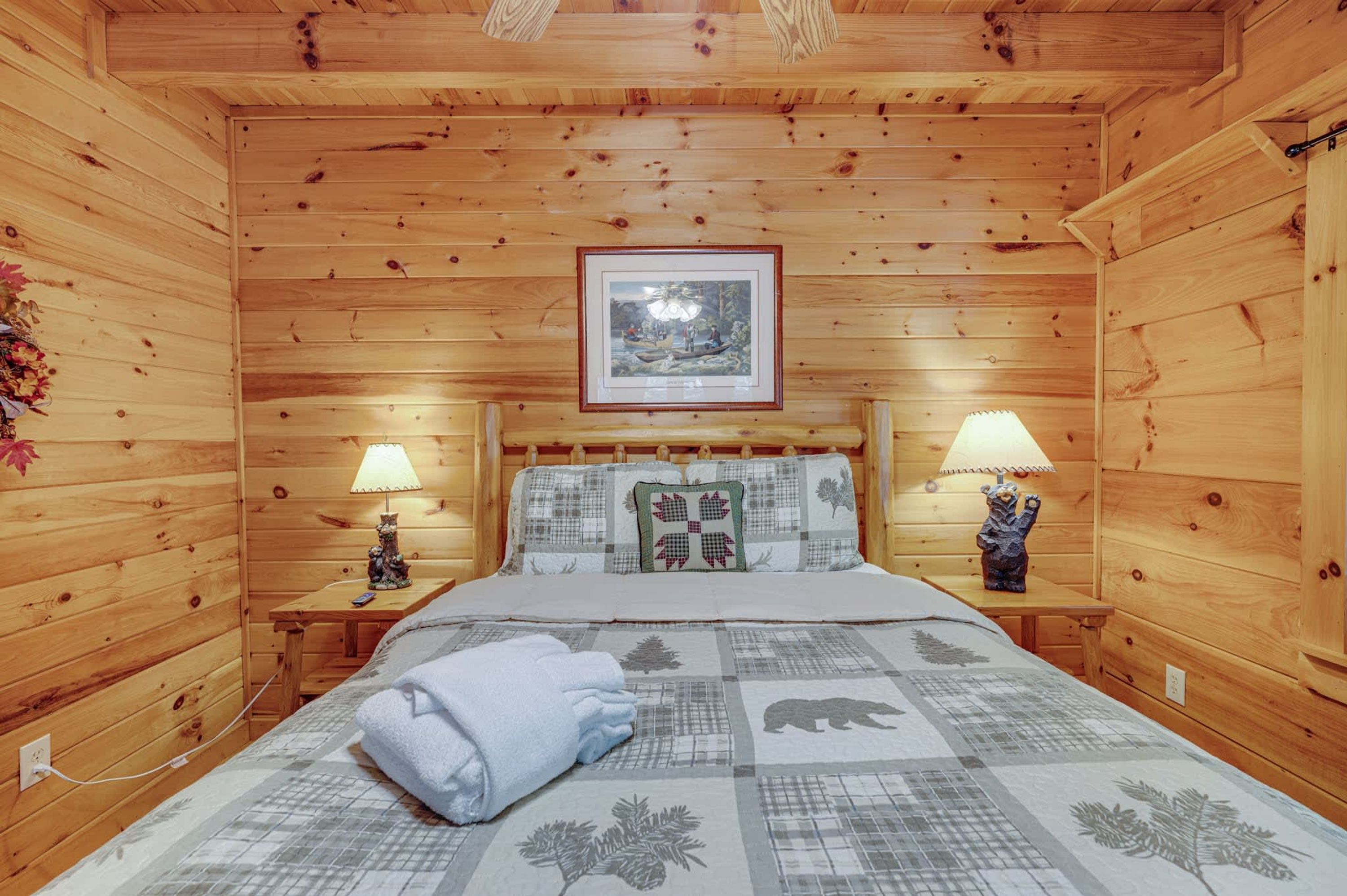 A cozy wooden room with a bed, two nightstands, a framed picture on the wall, and a quilt with animal prints.