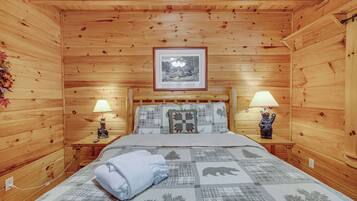 A cozy wooden room with a bed, two nightstands, a framed picture on the wall, and a quilt with animal prints.