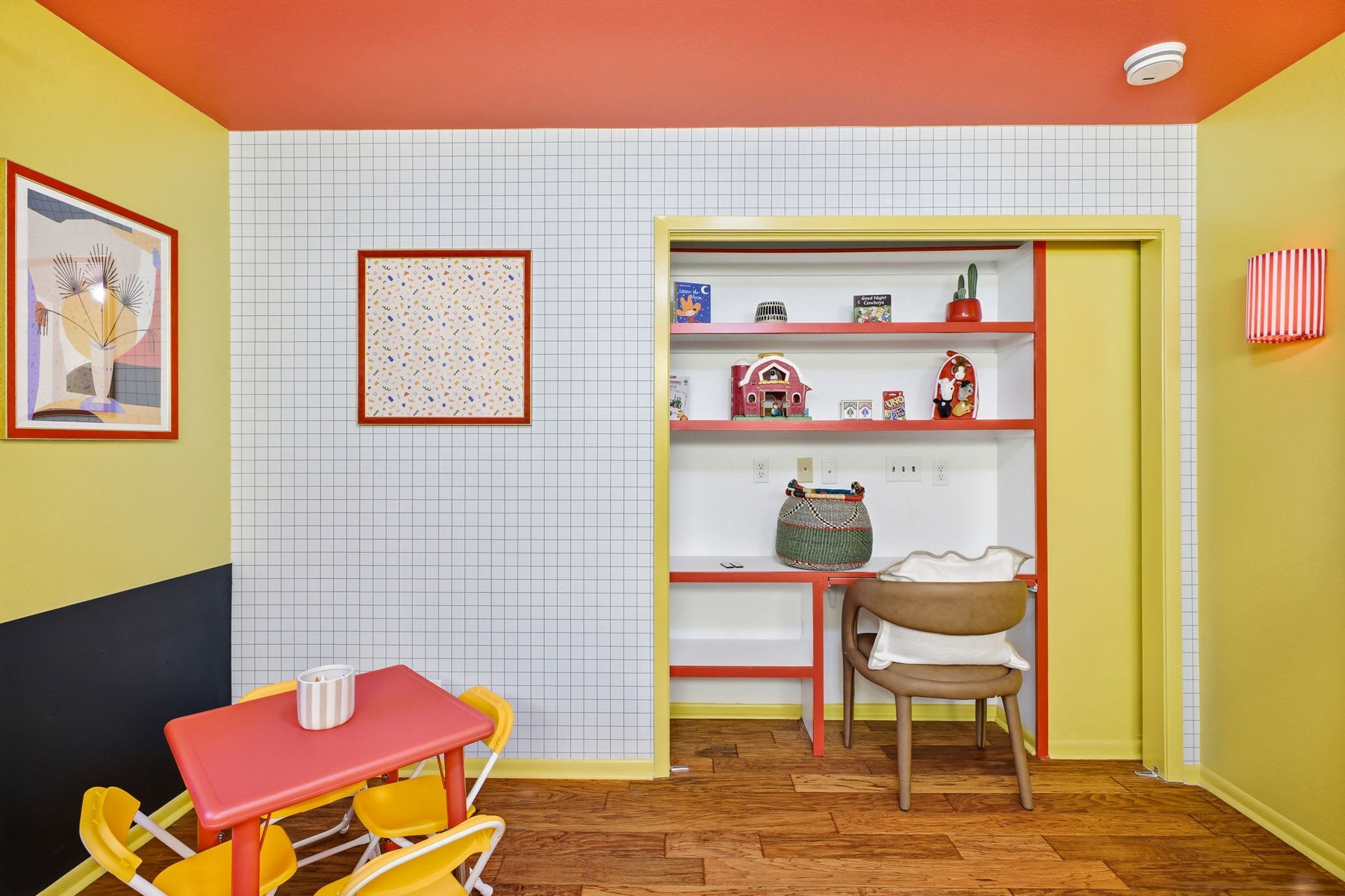 A room with a dining table and chairs, a bookshelf with various items, and a door leading to another room.