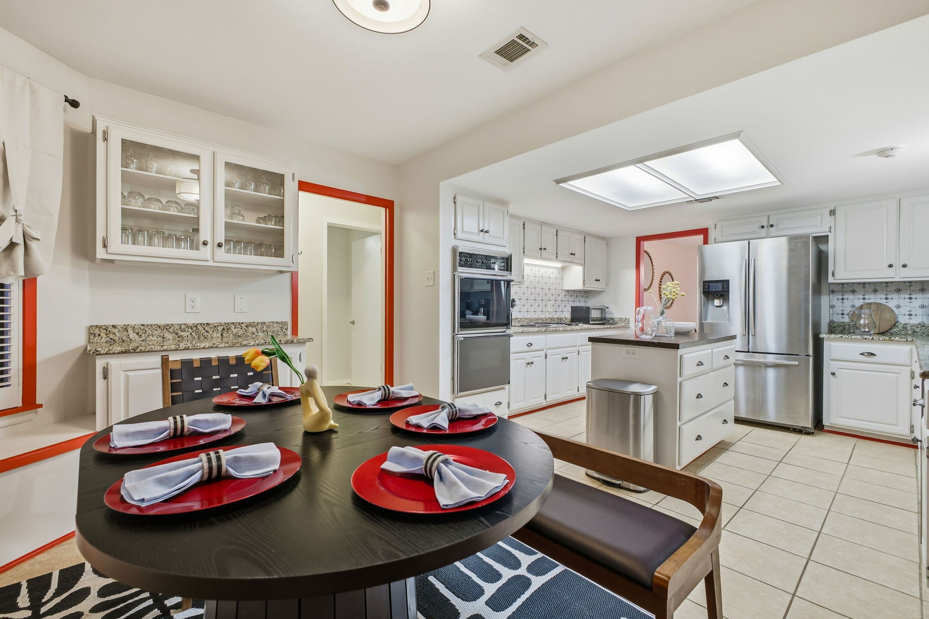 A modern kitchen with white cabinets, stainless steel appliances, and a dining area with a round table set for four.