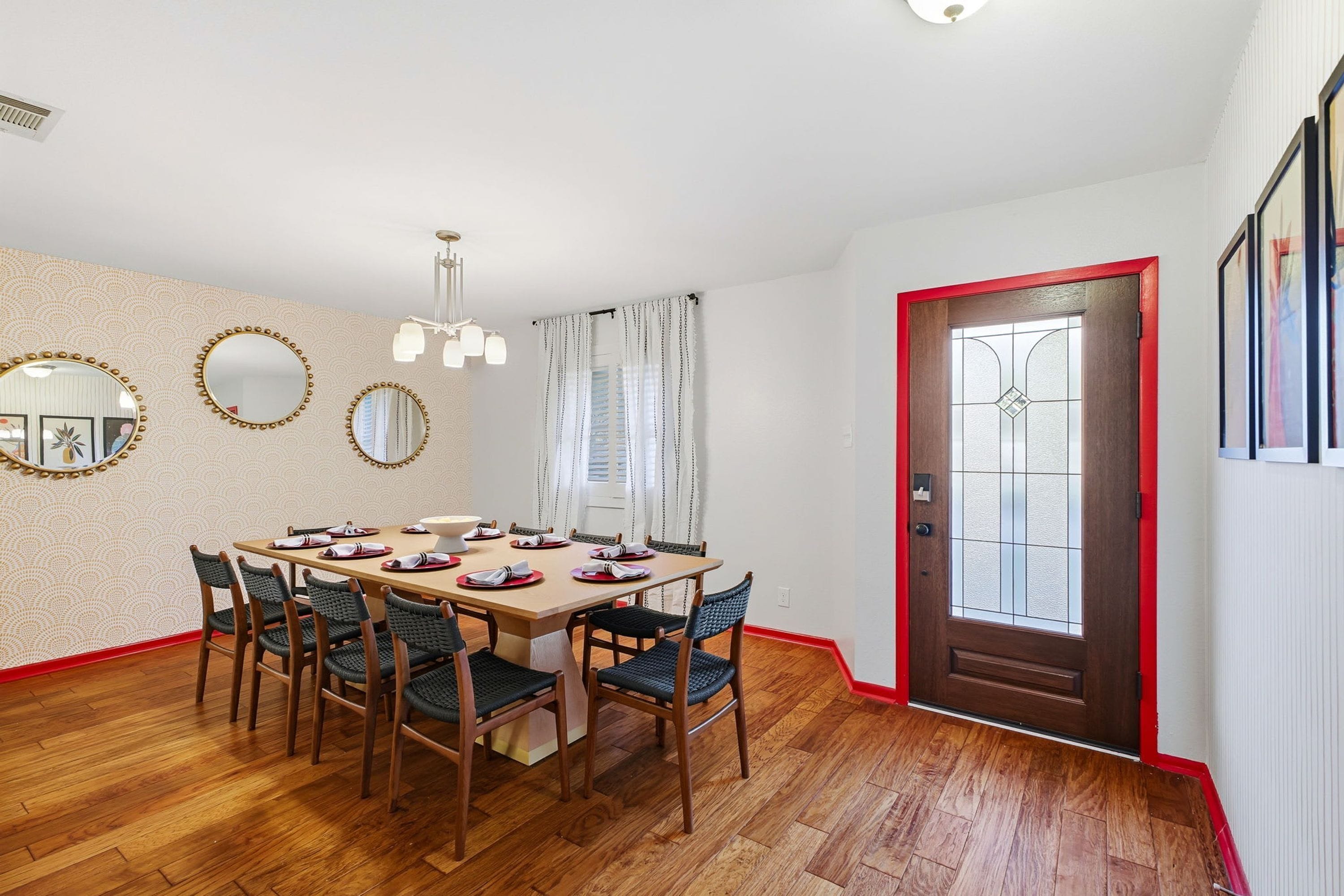 Een eetkamer met een houten tafel gedekt voor vier personen, omringd door stoelen, een behanget en een deur met een rode omlijsting.