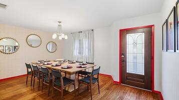 A dining room with a wooden table set for four, surrounded by chairs, a patterned wall, and a door with a red frame.