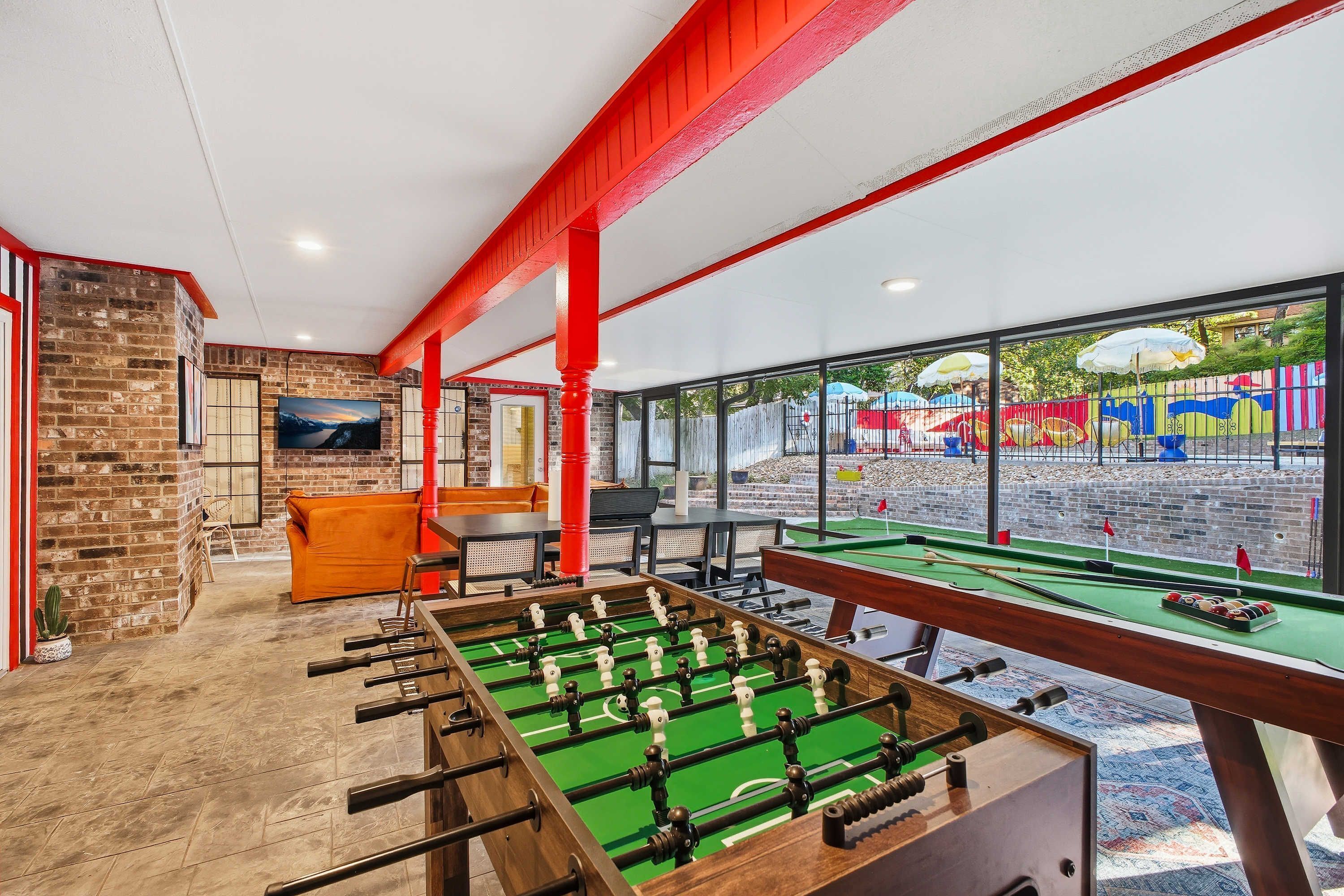 A room with a foosball table, a brick wall, and a television.