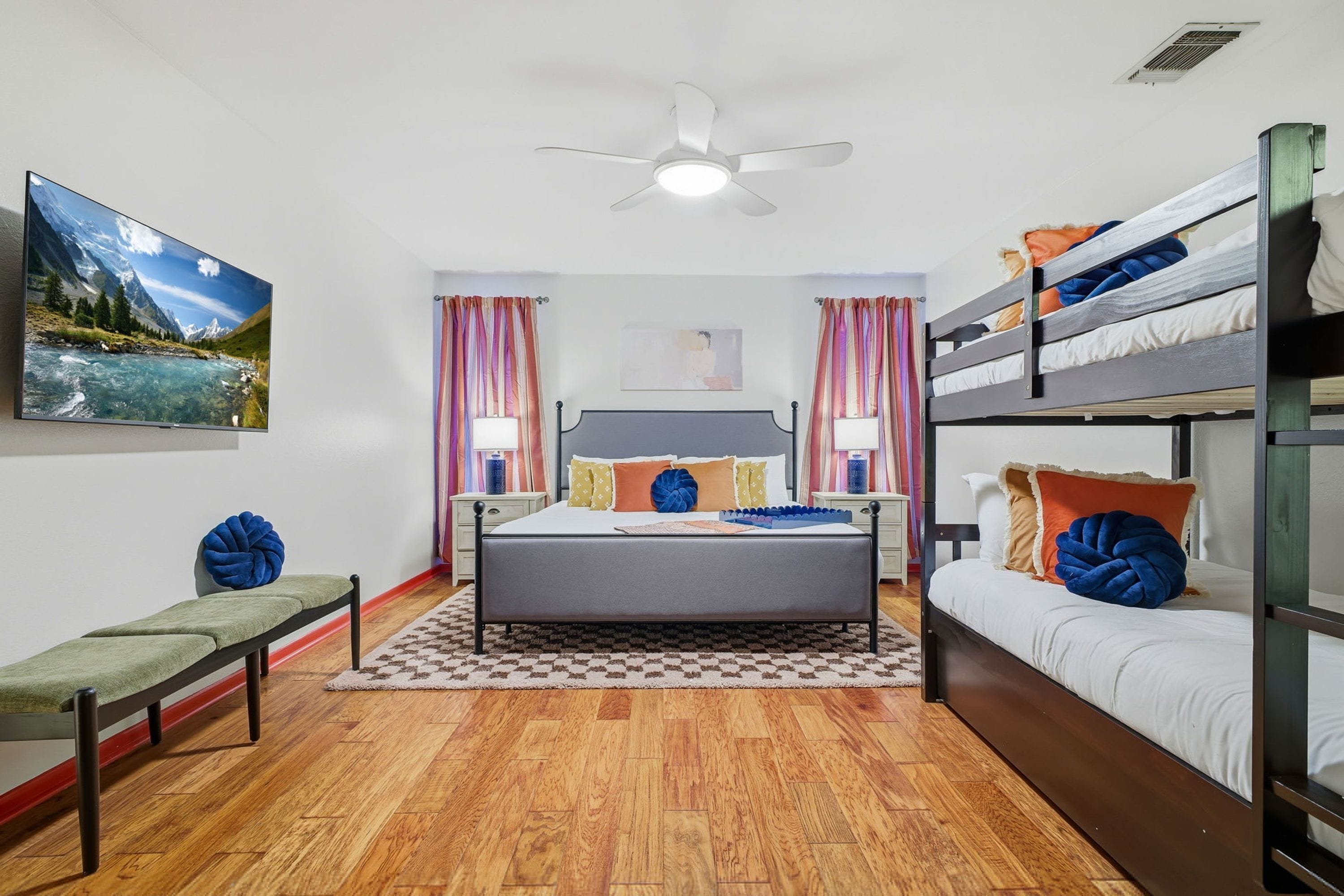 A bedroom with a bed, a bench, a bunk bed, a ceiling fan, and a painting on the wall.