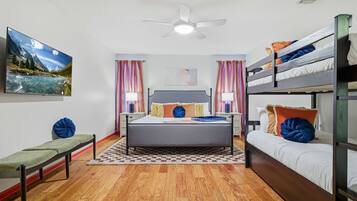 A bedroom with a bed, a bench, a bunk bed, a ceiling fan, and a painting on the wall.