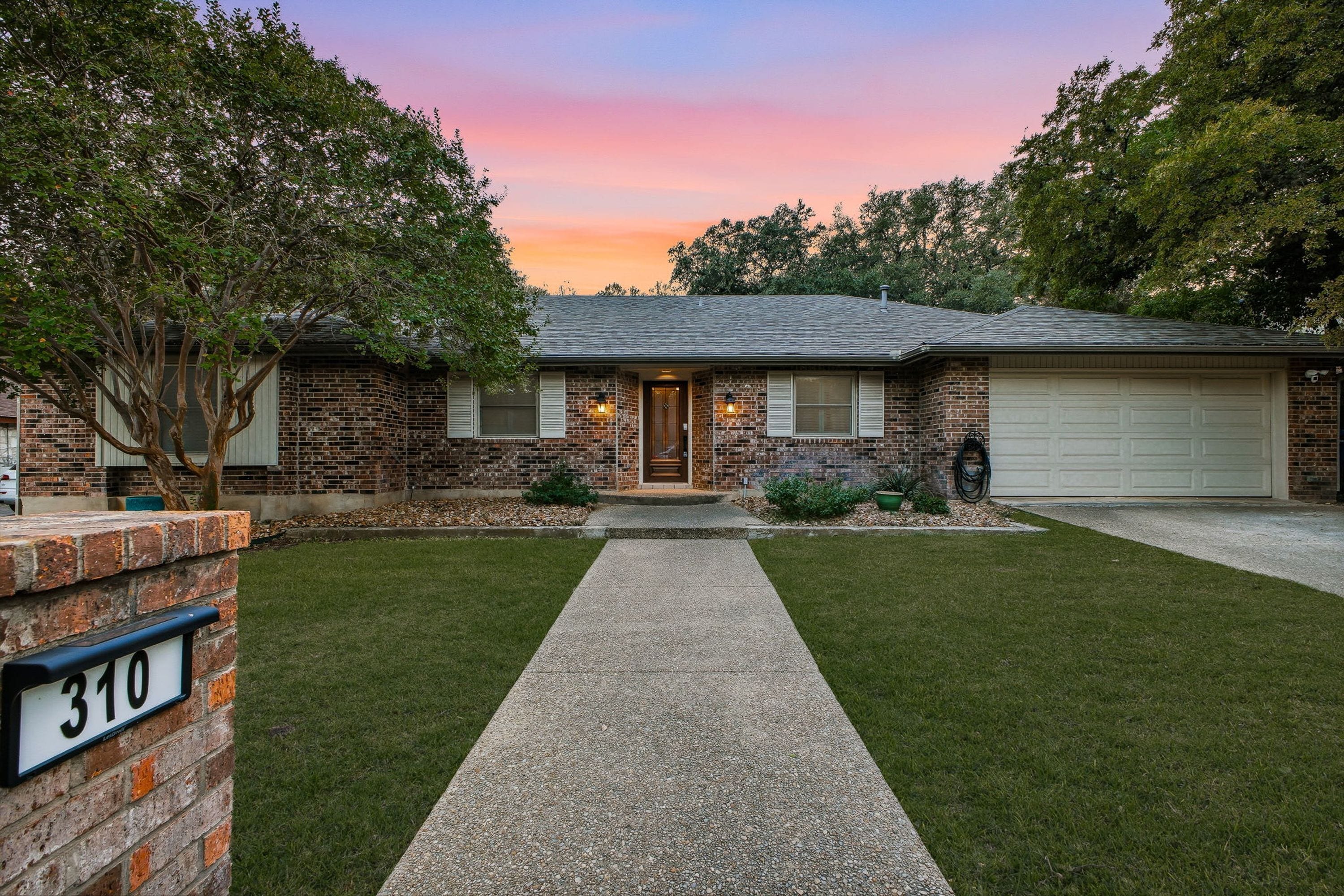 A two-story brick house with a front porch, a driveway, and a well-maintained lawn.