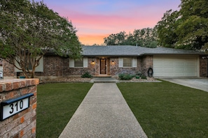 A two-story brick house with a front porch, a driveway, and a well-maintained lawn. - Sleeps 16 Heated Pool Hot Tub Sport Court (San Antonio)