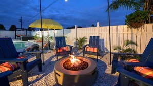 An outdoor patio area with a fire pit, lounge chairs, and string lights. - Backyard Oasis Pool Hot Tub Putt Putt Bar (Largo)