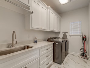 A kitchen with white cabinets, a stainless steel sink, a built-in oven, and a red vacuum cleaner. - House at the Refuge - Relax Take in Nature (Medicine Park)