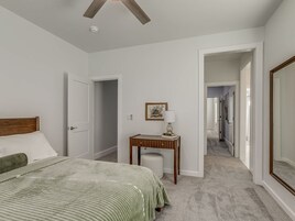 A bedroom with a bed, a desk, and a hallway leading to another room.