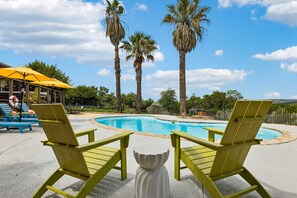 A poolside area with two green lounge chairs facing the pool, surrounded by palm trees and a clear sky. - The Lakeside Soundtrack Pool Hot Tub Games (Spicewood)