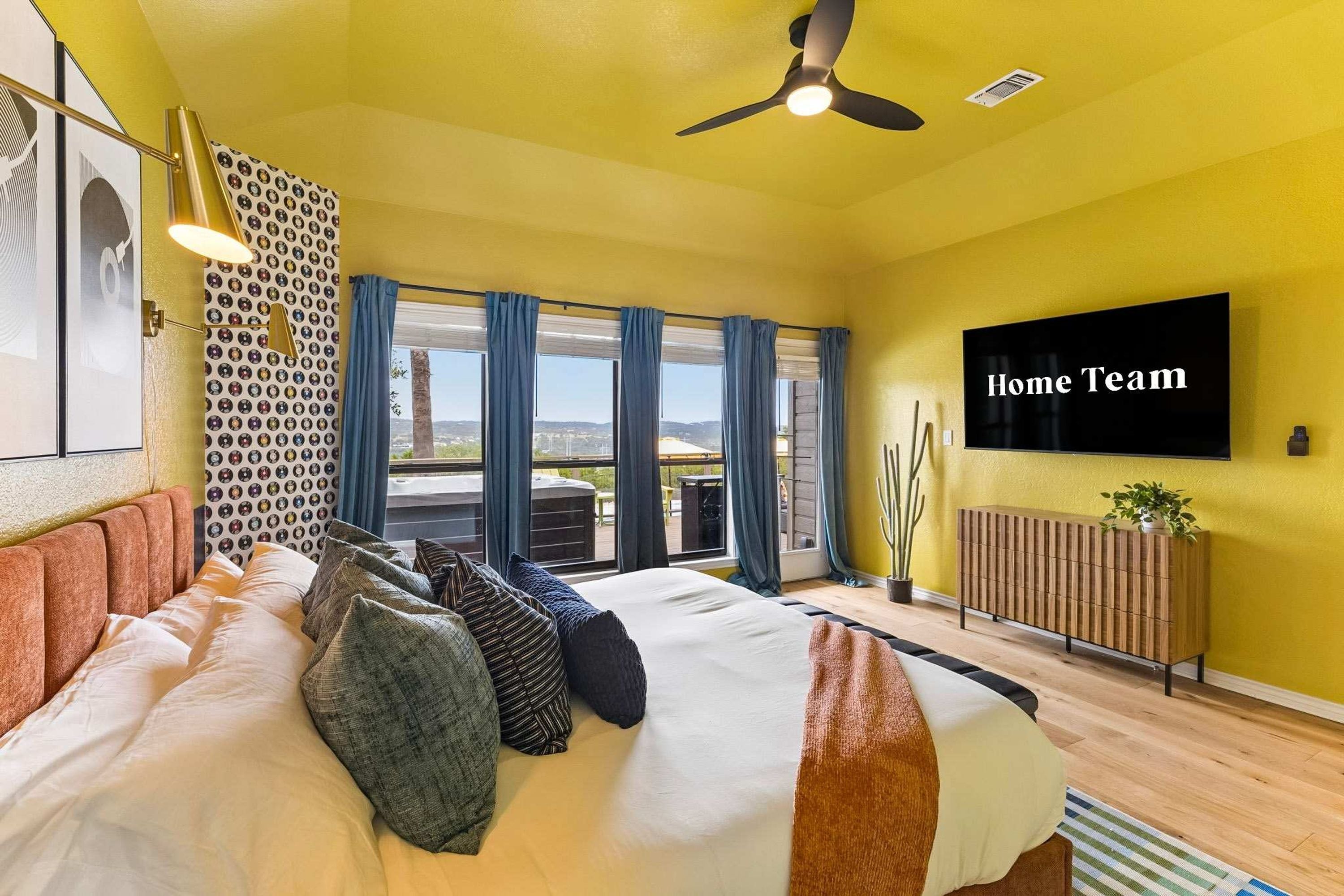 A hotel room with a bed, a ceiling fan, a TV, and a view of the outdoors.