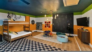 Una habitación con literas, una mesa con sillas, una pared con pizarra y un televisor.