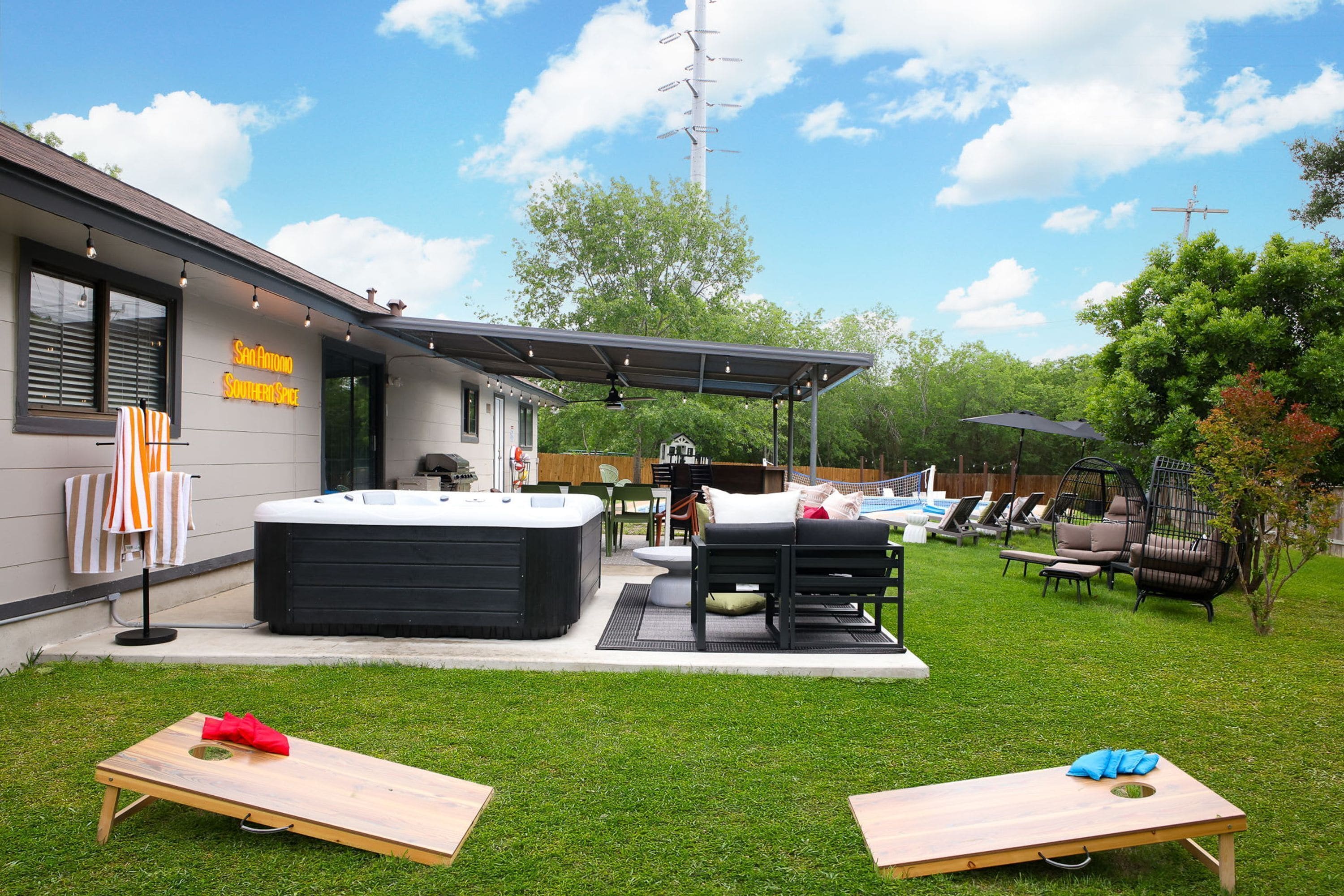 A modern outdoor patio with a hot tub, seating area, and a sign for 'San Antonio Southern Spice'.