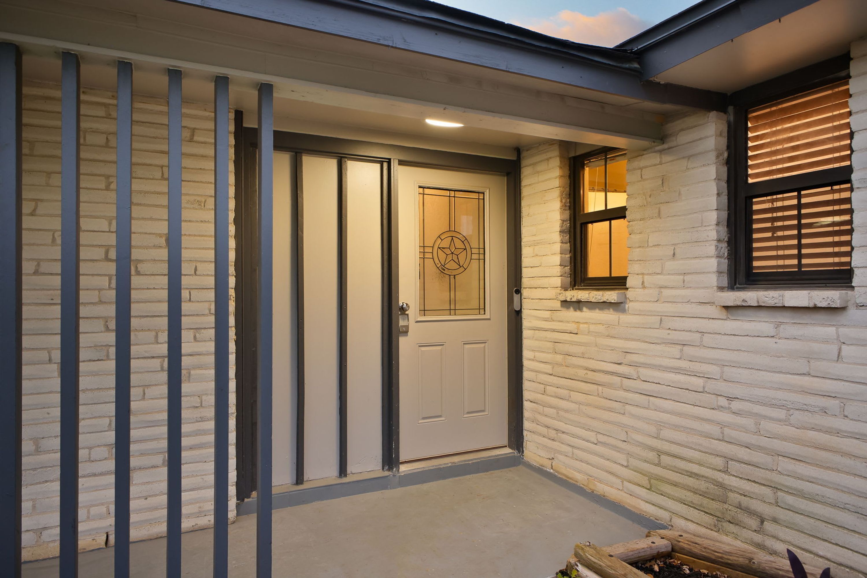 Una entrada de vivienda con puerta blanca, un ventanal pequeño con persianas y un área de porche de hormigón.