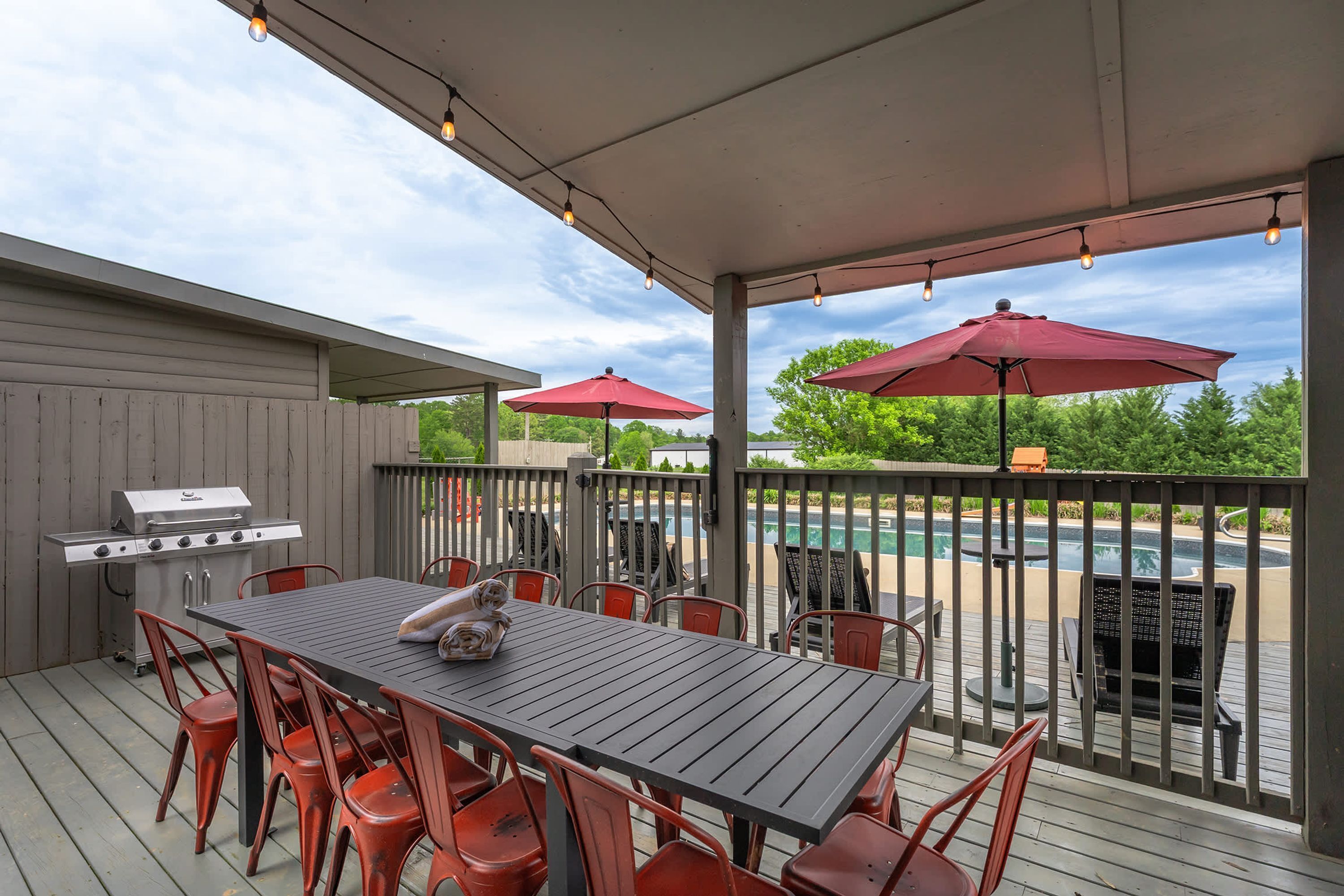 Een terras buiten met een barbecue, eettafel, stoelen en parasols.