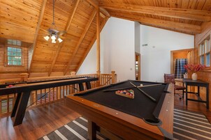 A pool table in a room with wooden walls and a sloped ceiling.