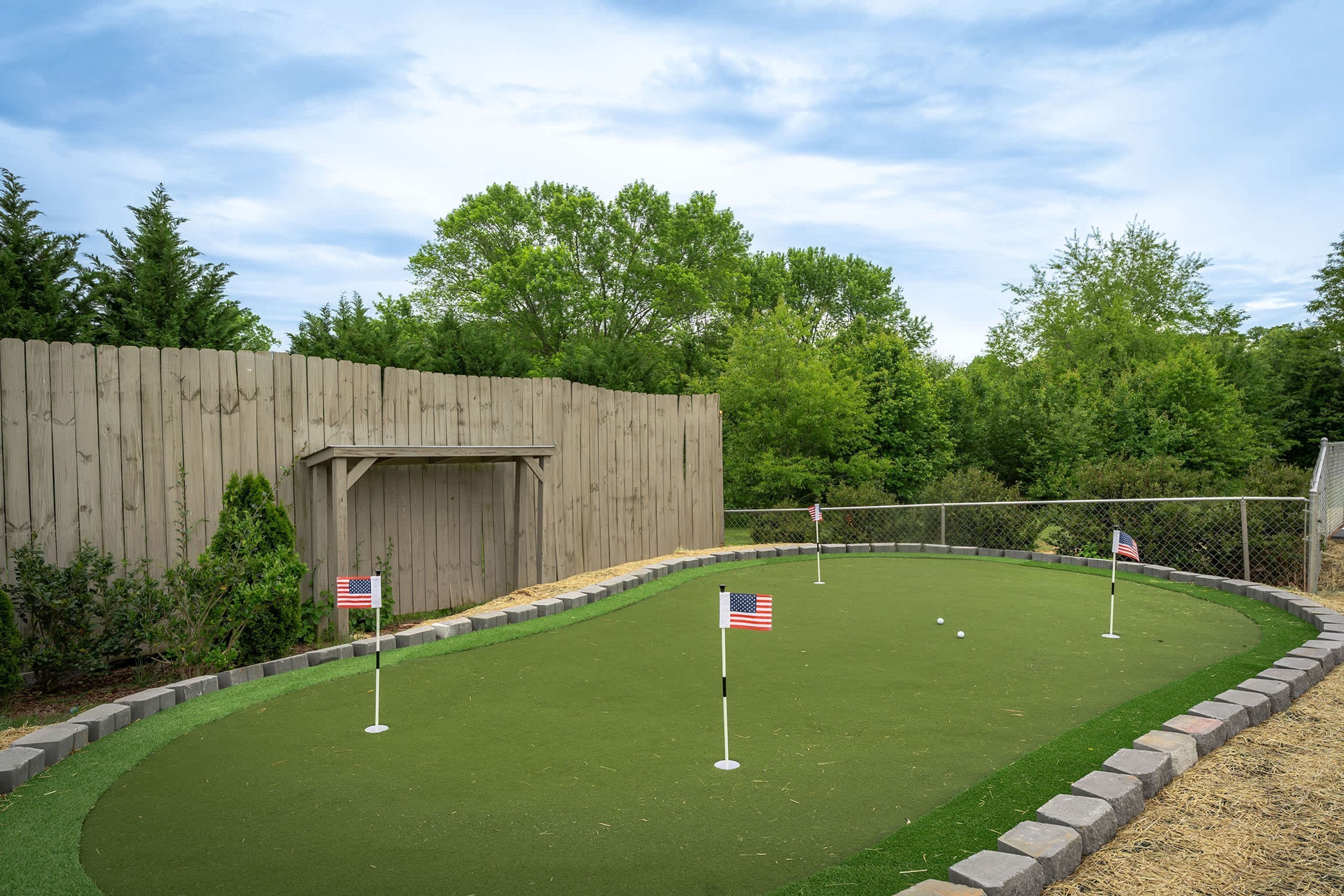 A miniature golf course with American flags marking the holes, surrounded by a wooden fence and greenery.