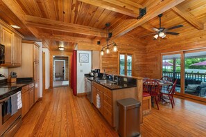 A spacious kitchen with wooden cabinetry, a central island, and a dining area with red chairs. - 7 Br Sleeps 20 Sport Court Pool Hot Tub Playground (Arden)