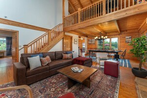 A spacious living room with a wooden staircase, a dining area, and a view of the outdoors.