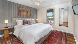 A bedroom with a bed, a nightstand, a floor lamp, a ceiling fan, a window with blinds, and a mirror on the wall. - 7 Br Sleeps 20 Sport Court Pool Hot Tub Playground (Arden)