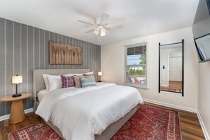 A bedroom with a bed, a nightstand, a floor lamp, a ceiling fan, a window with blinds, and a mirror on the wall. - 7 Br Sleeps 20 Sport Court Pool Hot Tub Playground (Arden)