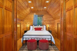 A wooden-paneled room with a bed, two nightstands, and a window with blinds.