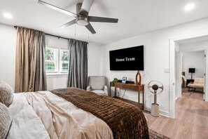 A modern bedroom with a bed, a desk, a chair, a TV, and a ceiling fan.