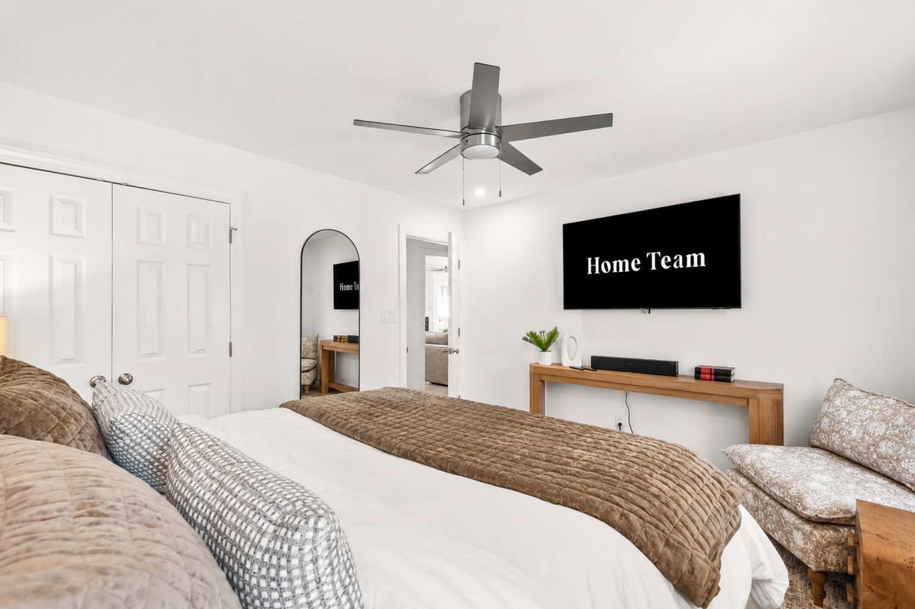 A bedroom with a bed, a desk, a chair, a TV, and a ceiling fan.