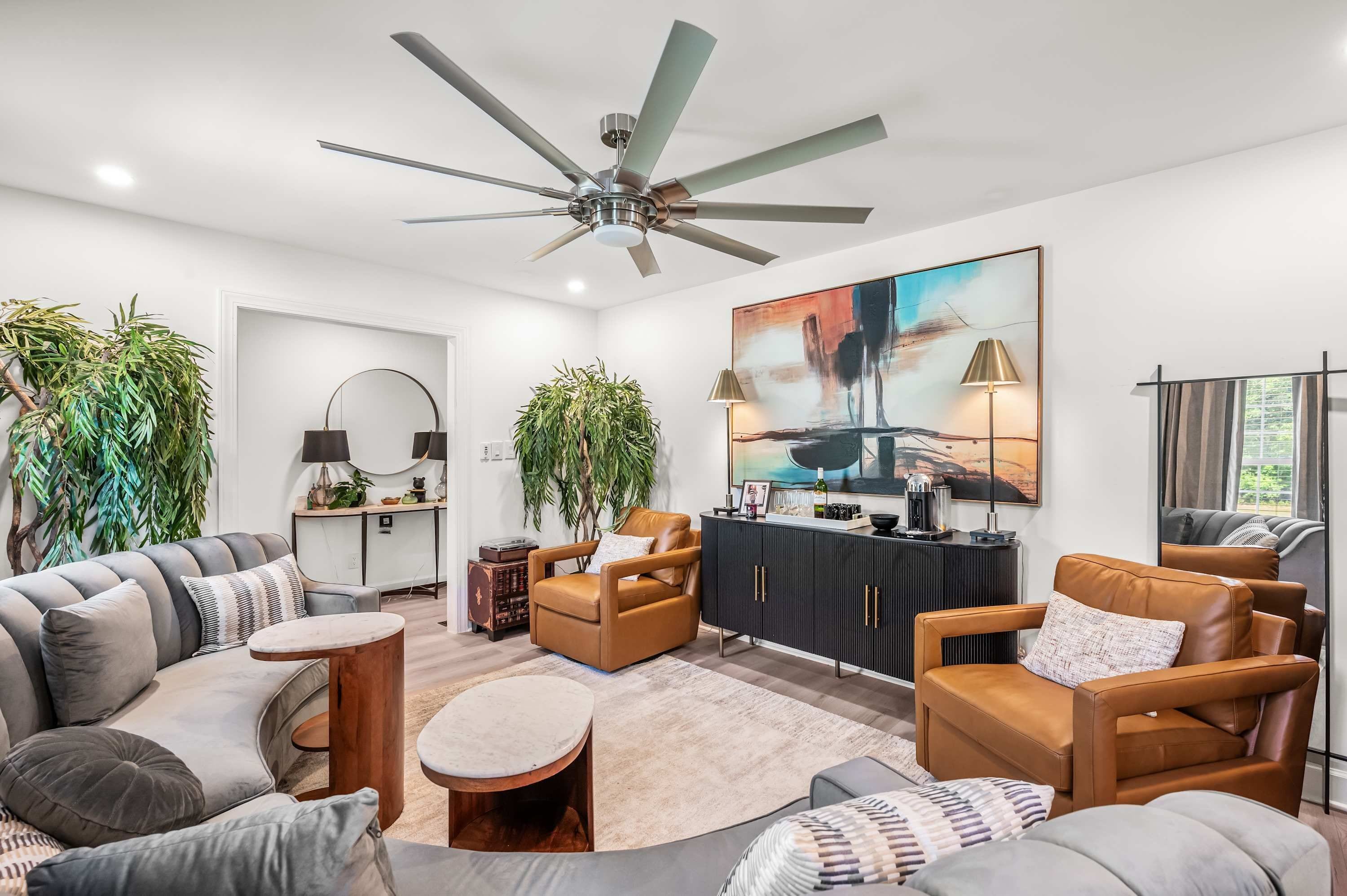 A modern living room with a ceiling fan, sofas, a coffee table, and a large abstract painting.