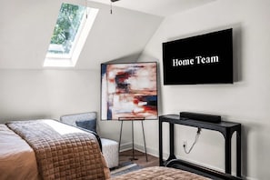 Ein modernes Schlafzimmer mit einem Bett, einem Stehpult, einem Fernseher und einem Bild an der Wand.