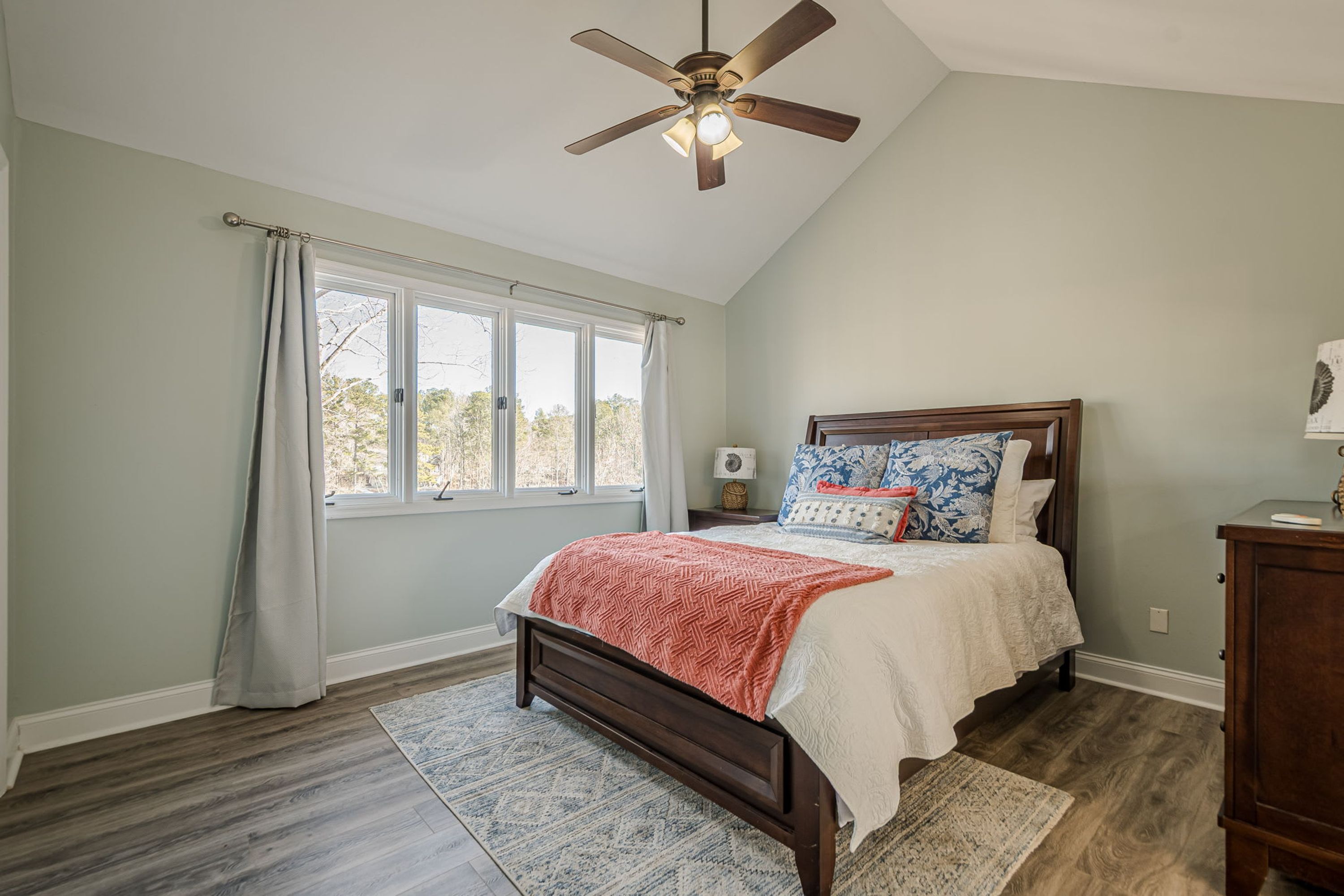 A bedroom with a bed, a ceiling fan, a window with curtains, a nightstand, and a dresser.