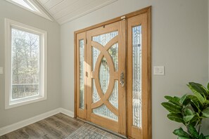 Eine Holztür mit Glasfeldern und einem Griff, ein Fenster mit Blick auf Bäume und ein Blumentopf.