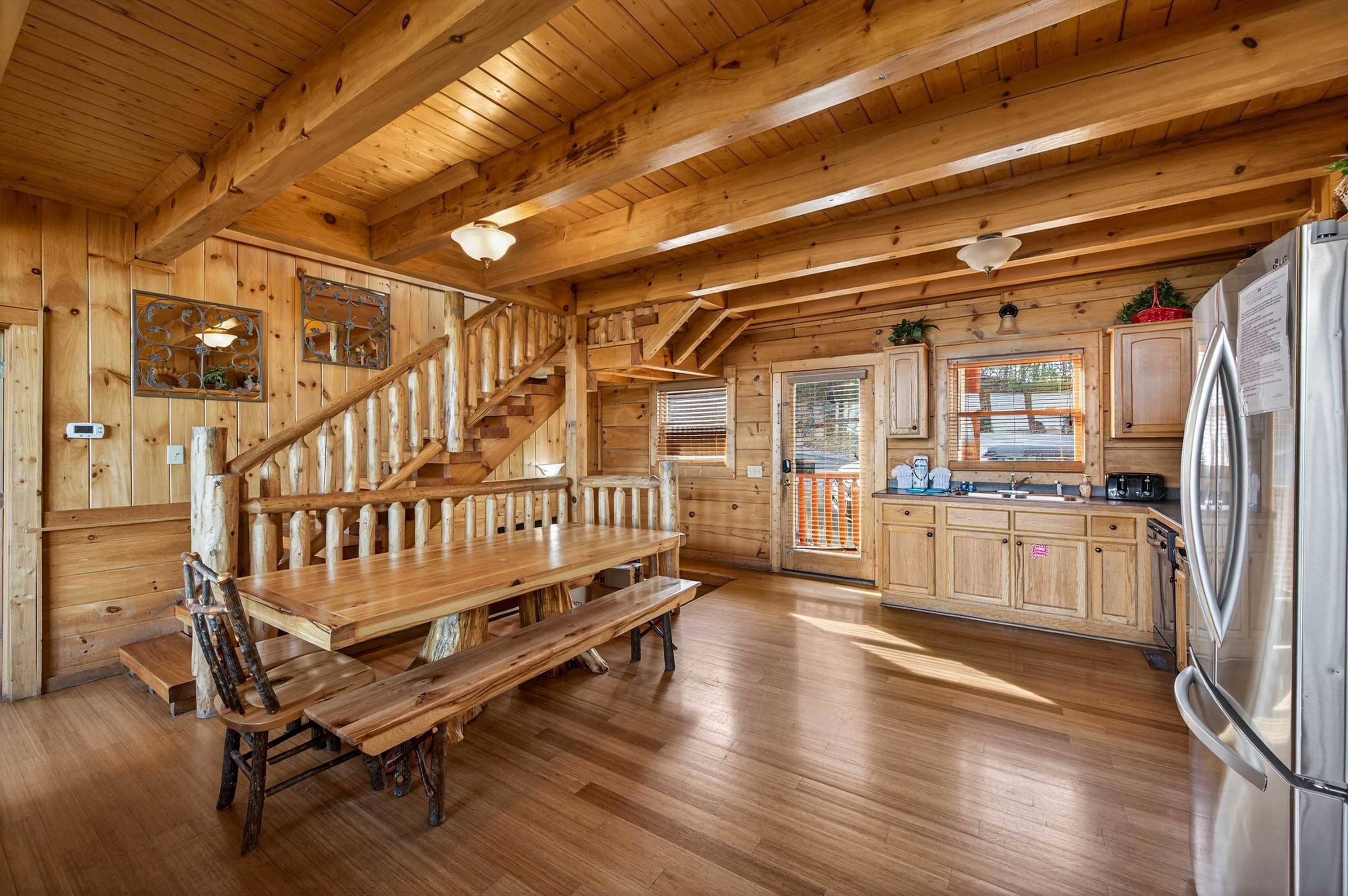 A wooden interior with a wooden staircase, a dining table with benches, and a kitchen area with cabinets and appliances.