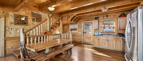 A wooden interior with a wooden staircase, a dining table with benches, and a kitchen area with cabinets and appliances.