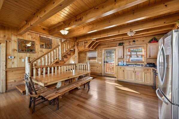 A wooden interior with a wooden staircase, a dining table with benches, and a kitchen area with cabinets and appliances. - Black Bear Escape Mtn Views Hot Tub Game Room (Sevierville)