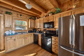 A kitchen with wooden cabinets, stainless steel appliances, and a window with blinds. - Black Bear Escape Mtn Views Hot Tub Game Room (Sevierville)