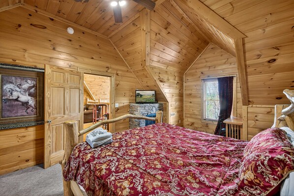 A wooden cabin bedroom with a bed, a television, and a painting on the wall. - Black Bear Escape Mtn Views Hot Tub Game Room (Sevierville)