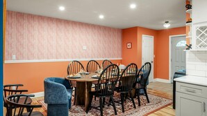 Un coin repas comprenant une table ronde, six chaises, un tapis à motifs, ainsi qu’un espace cuisine avec des placards et un plan de travail.
