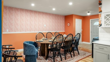 A dining area with a round table, six chairs, a patterned rug, and a kitchen area with cabinets and a countertop.