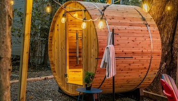 A wooden barrel structure with an open door, a small table with a plant, and a towel hanging on a hook.