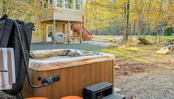 A hot tub in a backyard with a wooden deck, a covered patio, and a house in the background.