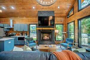 Un interior de cabaña acogedor con chimenea de piedra, techo de madera y ventanas amplias.