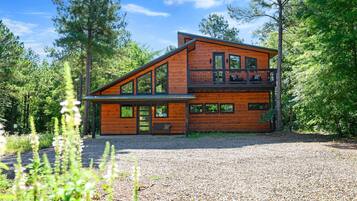 A two-story wooden cabin with a balcony, surrounded by trees.