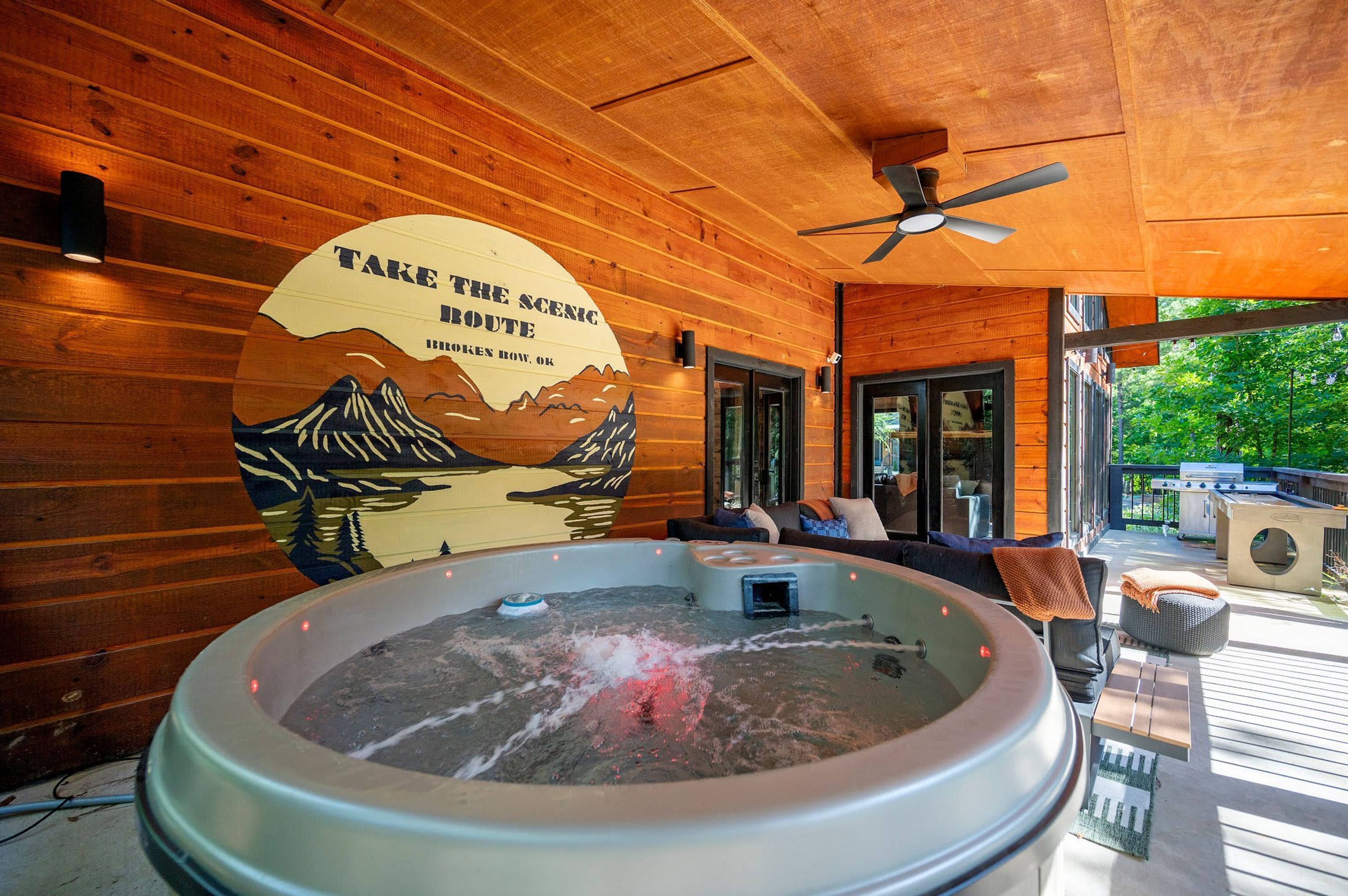 A wooden cabin interior with a hot tub, a ceiling fan, and a scenic route sign on the wall.