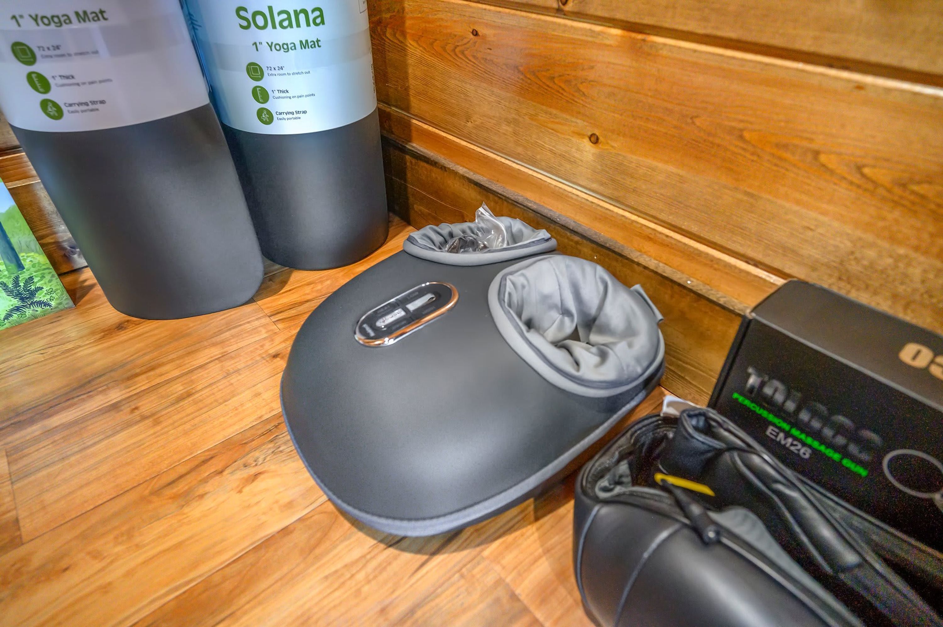 A yoga mat, a carrying strap, and a portable massage gun on a wooden floor.