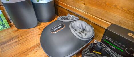 A yoga mat, a carrying strap, and a portable massage gun on a wooden floor.