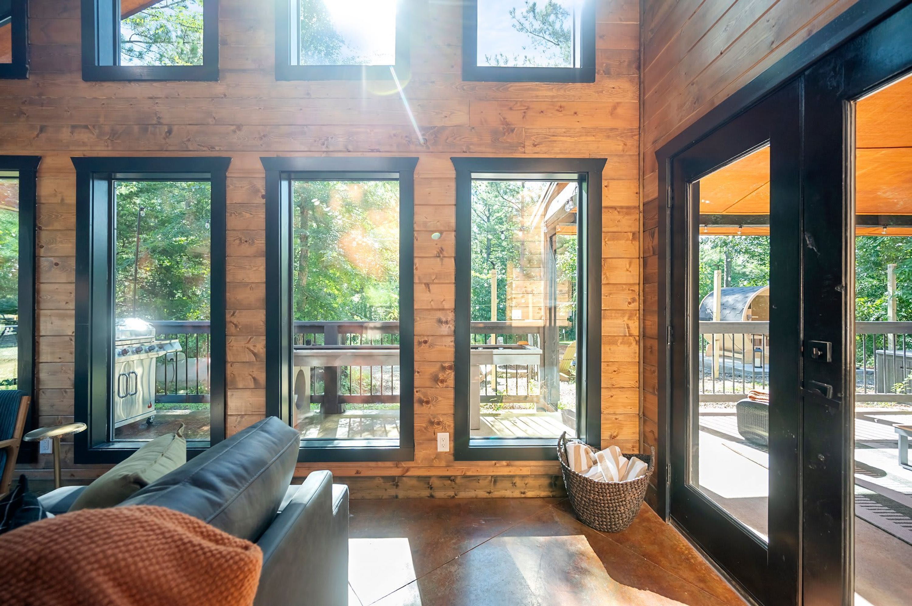 Interior moderno de una cabaña de troncos con un sofá de cuero, ventanas amplias y vistas al exterior.