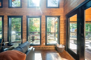 A modern log cabin interior with a leather sofa, large windows, and a view of the outdoors.